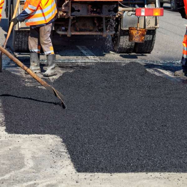 The road workers updating part of the road with fresh hot asphalt and smoothes it for repair